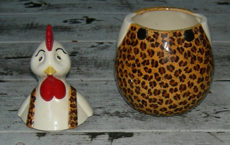 Puede incluir: Una jarra de galletas de cer&aacute;mica con forma de gallo con un dise&ntilde;o de estampado de leopardo. El gallo tiene una cresta y una papada rojas, plumas blancas y un babero de estampado de leopardo negro y marr&oacute;n.