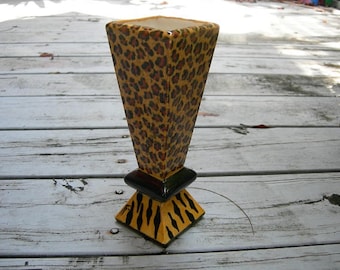 Peut inclure: Un vase en céramique avec un motif léopard et une base rayée noir et blanc. Le vase est posé sur une surface en bois.