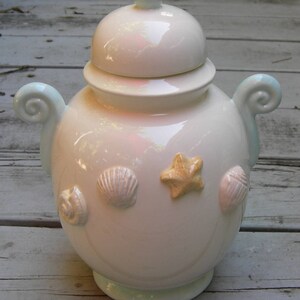 May include: White ceramic jar with a lid and a blue rim. The jar is decorated with seashells and a starfish.