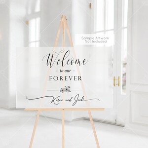 以下が含まれることがあります： 「Welcome - to our - FOREVER Karen and Jack」と黒の書体で書かれた白いウェルカムサイン。サインは木製イーゼルの上に置かれています。