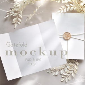 Puede incluir: Una maqueta de invitación plegable blanca con el texto "Gatefold mockup PSD & JPG 10x7". La invitación cerrada está atada con hilo y sellada con un sello de cera beige redondo. Acentos florales blancos están dispuestos alrededor.