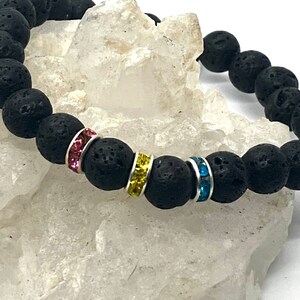 A black lava rock bracelet with three spacer beads are decorated in pink, yellow, and blue rhinestones.