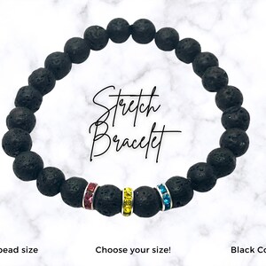 Black stretch bracelet with pink, yellow and blue crystal accents. The bracelet is made of 8mm lava rock beads. The text 'Stretch Bracelet' is written in white on a white marble background. The text 'Choose your size!' is written below the bracelet. The text 'Black Cording' is written below the bracelet. The text '8mm bead size' is written below the bracelet.
