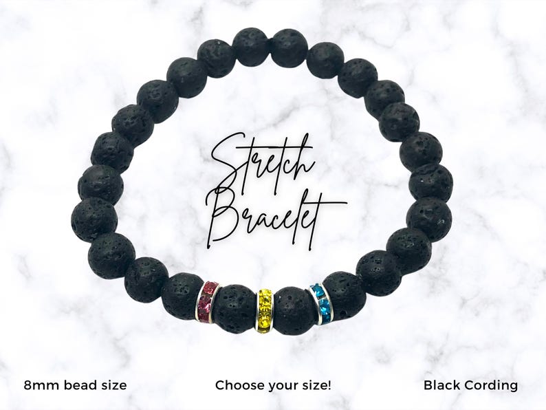 Black stretch bracelet with pink, yellow and blue crystal accents. The bracelet is made of 8mm lava rock beads. The text 'Stretch Bracelet' is written in white on a white marble background. The text 'Choose your size!' is written below the bracelet. The text 'Black Cording' is written below the bracelet. The text '8mm bead size' is written below the bracelet.