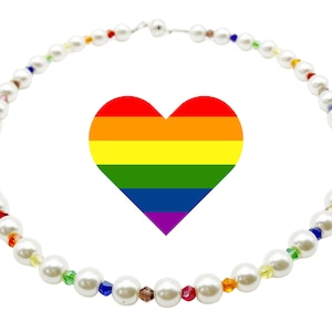 May include: A circular necklace featuring white faux pearls interspersed with small, multi-coloured faceted beads in red, orange, yellow, green, blue, and purple. A large, flat, heart-shaped graphic with horizontal rainbow stripes is centred within the necklace.