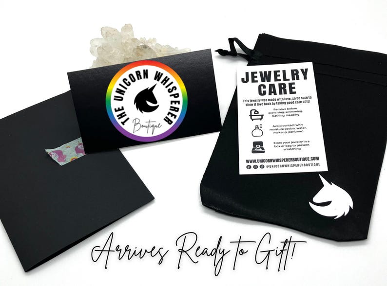 May include: A black drawstring jewellery pouch with a white unicorn logo, a black business card featuring a rainbow circular logo with the text The Unicorn Whisperer Boutique, and a white jewellery care instruction card with black text.