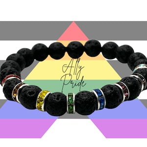 May include: Black lava rock bracelet with rainbow colored crystal beads. The bracelet is on a background of the Ally Pride flag.