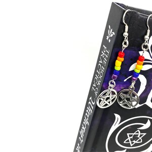 May include: A pair of drop earrings featuring silver-toned pentacle charms suspended from silver hooks. Each earring includes a vertical row of small, vibrant glass beads in a rainbow sequence of red, orange, yellow, green, blue, and purple.
