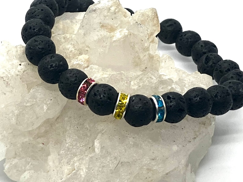 A black lava rock bracelet with three spacer beads are decorated in pink, yellow, and blue rhinestones.