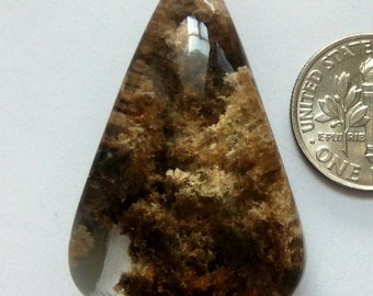 Könnte beinhalten: Ein klarer Quarz-Cabochon mit braunen und goldenen Einschlüssen. Der Cabochon ist tropfenförmig und etwa 2,5 cm lang.