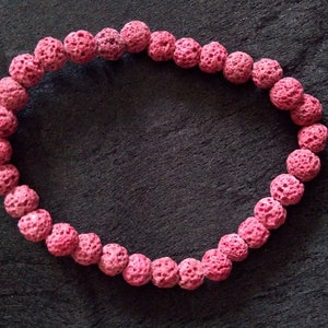 Peut inclure: Un bracelet en perles de lave rose. Le bracelet est composé de petites perles rondes avec une surface rugueuse et texturée.