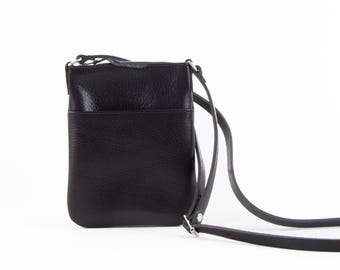 Op de afbeelding: Een zwarte leren crossbody tas met een lange, verstelbare riem. De tas heeft een rechthoekige vorm met een voorvak en een ritssluiting aan de bovenkant. Het leer heeft een getextureerde nerf.