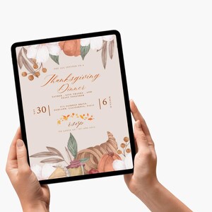 Op de afbeelding: Een tablet toont een uitnodiging voor een Thanksgiving-diner. Het ontwerp bevat aquarel illustraties van pompoenen, bloemen en een hoorn des overvloeds. De tekst bevat de datum, tijd en RSVP-informatie. De tablet wordt door twee handen vastgehouden.