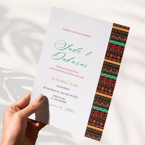 Könnte beinhalten: Eine Hochzeitskarte, gehalten von einer Hand, mit den Namen "Jade & Dakarai" in Schreibschrift. Die Einladung enthält Datum, Uhrzeit und Ort, mit einem dekorativen Rand aus geometrischen Mustern in Rot, Grün, Orange und Schwarz.