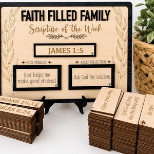 May include: A wooden display board with black and natural wood tones featuring the text FAITH FILLED FAMILY, Scripture of the Week, JAMES 1:5, KIDS VERSION, God helps me make good choices, ADULT REFLECTION, and Ask God for wisdom, with stacks of wooden tiles.