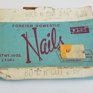 Puede incluir: Una caja azul y blanca de clavos de 8d cortados a 2-1/2 pulgadas. La caja está etiquetada como "Foreign Domestic Nails" y "USI". El peso neto es de 16 onzas (1 libra).