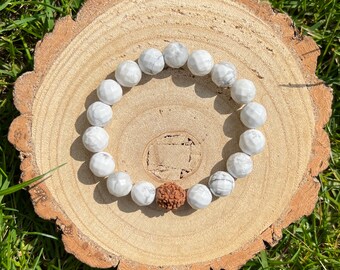 May include: White Howlite beaded bracelet with a brown Rudraksha bead. The bracelet is on a wooden surface.