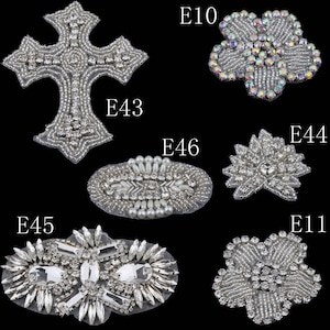 May include: Six different rhinestone embellishments for clothing or crafts. The embellishments are in the shapes of a cross, a flower, a leaf, an oval, a starburst, and a heart. The embellishments are all silver and have clear rhinestones.