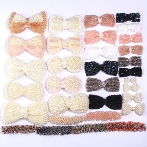 May include: Assortment of beaded hair bows in various colors and styles, including white, black, brown, and pink. The bows are made with small beads and some have a ribbon center. There are also several strands of beads in different colors.