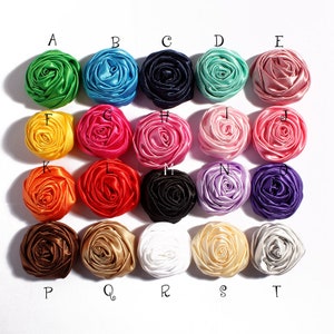 May include: Twenty assorted satin fabric rosettes in various colors, including green, blue, pink, yellow, orange, red, black, purple, brown, and white. Each rosette is approximately 2 inches in diameter.