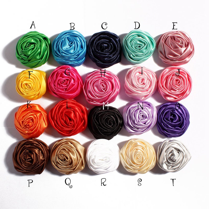 May include: Twenty assorted satin fabric rosettes in various colors, including green, blue, pink, yellow, orange, red, black, purple, brown, and white. Each rosette is approximately 2 inches in diameter.