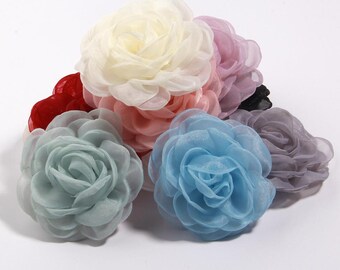 Puede incluir: Una colección de adornos florales de tela en varios colores, incluyendo rojo, crema, rosa, azul claro y lavanda. Las flores tienen múltiples capas de pétalos, creando una apariencia completa y realista. Estas flores decorativas son adecuadas para manualidades y accesorios.
