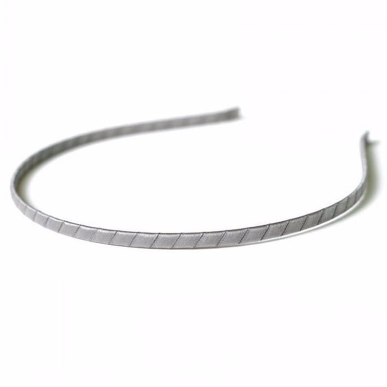 May include: A silver headband with a textured, patterned design.