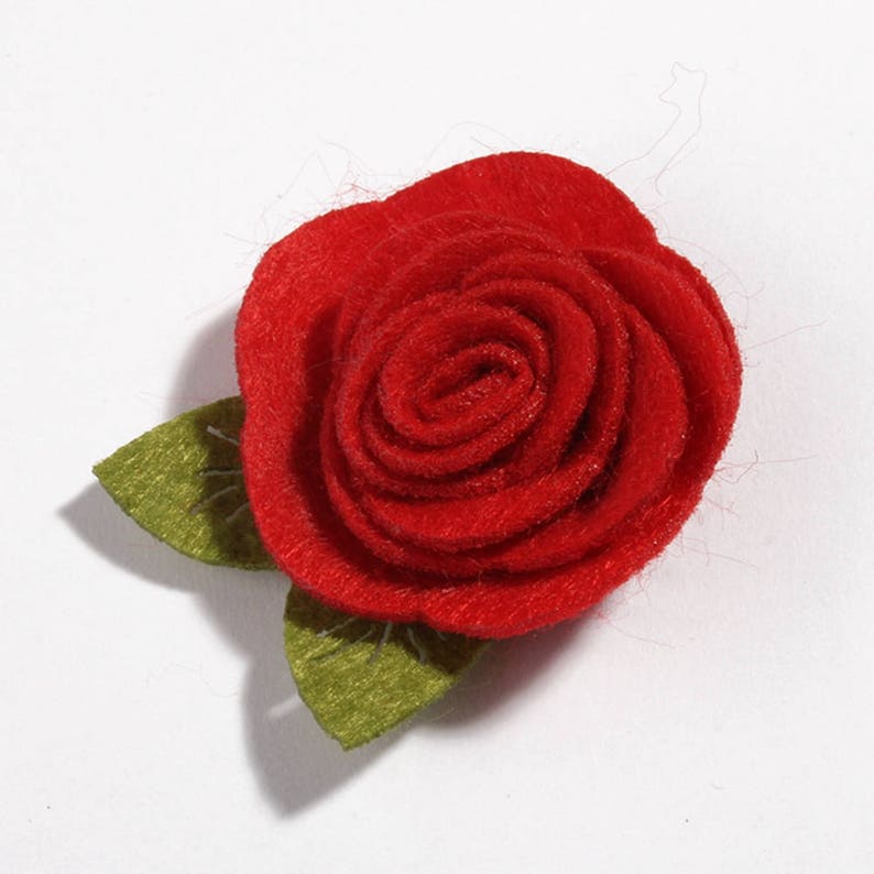 K&ouml;nnte beinhalten: Eine handgefertigte rote Filzrose mit zwei gr&uuml;nen Bl&auml;ttern. Die Rose steht in voller Bl&uuml;te, mit eng gewickelten Bl&uuml;tenbl&auml;ttern. Die Bl&auml;tter sind ein ged&auml;mpftes Gr&uuml;n und bilden einen Kontrast zur leuchtend roten Bl&uuml;te. Geeignet f&uuml;r Bastelarbeiten.
