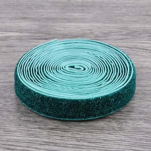 Puede incluir: Un rollo de el&aacute;stico azul turquesa con un acabado de purpurina verde. El el&aacute;stico est&aacute; enrollado y listo para ser utilizado para coser o proyectos de manualidades.