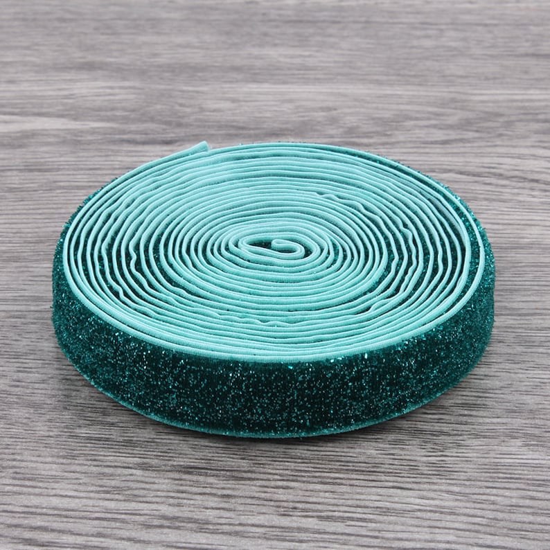 Puede incluir: Un rollo de el&aacute;stico azul turquesa con un acabado de purpurina verde. El el&aacute;stico est&aacute; enrollado y listo para ser utilizado para coser o proyectos de manualidades.