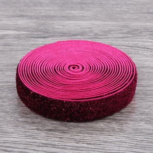 Puede incluir: Un rollo de cinta el&aacute;stica rosa con purpurina. La cinta est&aacute; enrollada y tiene un acabado brillante.