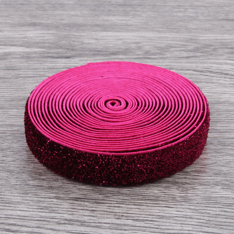 Puede incluir: Un rollo de cinta el&aacute;stica rosa con purpurina. La cinta est&aacute; enrollada y tiene un acabado brillante.