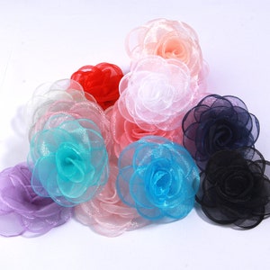 May include: Assortment of colorful fabric flower embellishments in various shades of pink, blue, purple, red, and black. The flowers are made of layered tulle and have a delicate, feminine appearance.