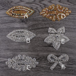 Könnte beinhalten: Sechs verschiedene Strass-Verzierungen in Silber und Gold. Die Verzierungen haben die Form eines Blattes, einer Blume, einer Schleife und zweier Ovale. Die Verzierungen haben einen Durchmesser von etwa 4,95 cm bis 7,3 cm.