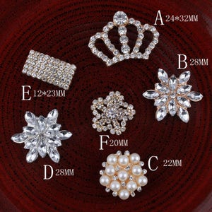 Pode incluir: Conjunto de seis enfeites de strass e pérolas em vários formatos e tamanhos. Os enfeites estão sobre um fundo vermelho. Os enfeites são etiquetados com as letras A a F e as medidas em milímetros.