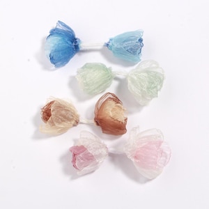 Könnte beinhalten: Draufsicht auf sechs handgefertigte Stoffblumen, paarweise angeordnet. Jede Blume ist durch einen dünnen, weißen Stiel verbunden. Die Blumen sind in den Farbtönen Blau, Grün, Beige und Rosa gehalten und haben ein durchscheinendes, geschichtetes Aussehen.