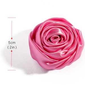 May include: A pink satin rose flower measuring 5 cm (2 inches) in diameter. The rose is made of fabric and has a realistic appearance.