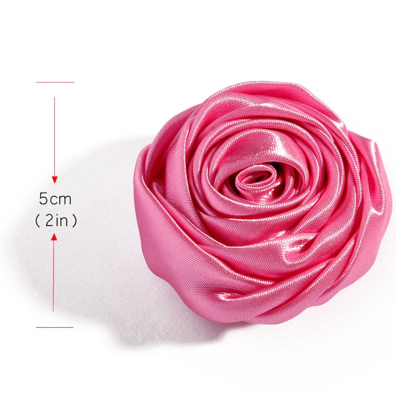 May include: A pink satin rose flower measuring 5 cm (2 inches) in diameter. The rose is made of fabric and has a realistic appearance.