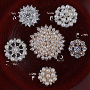 Op de afbeelding: Assortiment van zes parel- en strassversieringen in verschillende maten en stijlen. De versieringen zijn gerangschikt op een houten oppervlak. De versieringen zijn gelabeld met de letters A tot en met F en hun bijbehorende afmetingen in millimeters.