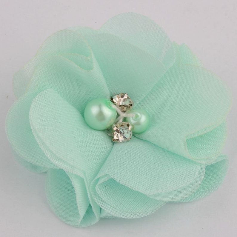 May include: A light green fabric flower with a pearl and rhinestone embellishment.