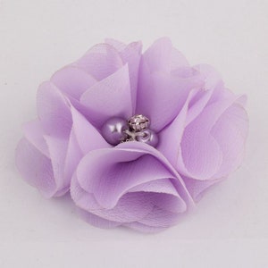 May include: A lavender fabric flower with a pearl and rhinestone embellishment. The flower is made of soft, layered fabric and has a delicate, feminine look.