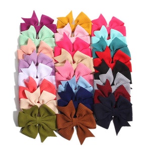May include: A collection of colorful hair bows in various shades, including pink, green, blue, and brown. The bows are arranged closely together, showcasing their textured fabric and bow design. The bows are a popular accessory for girls and women.
