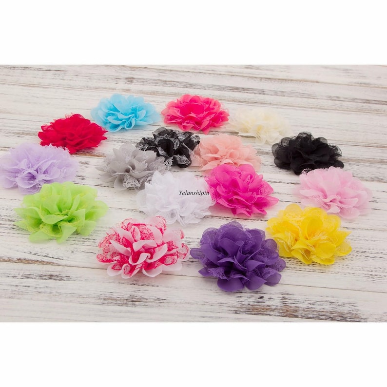 May include: Assortment of 14 small fabric flower embellishments in various colors, including pink, purple, yellow, green, white, and black. The flowers are made of a soft, layered fabric and have a delicate lace trim.