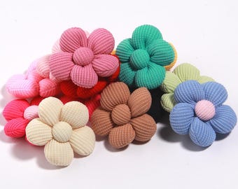 Puede incluir: Una colección de adornos florales de tela de pana colorida. Las flores son de varios tonos de rosa, rojo, verde, azul, beige y marrón. Cada flor tiene un centro redondo y pétalos acanalados.