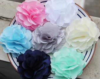 Puede incluir: Una colección de flores de tela en varios colores, incluyendo rosa, blanco, azul, gris, amarillo, azul marino y verde menta. Las flores están dispuestas en un plato blanco con rayas azules.
