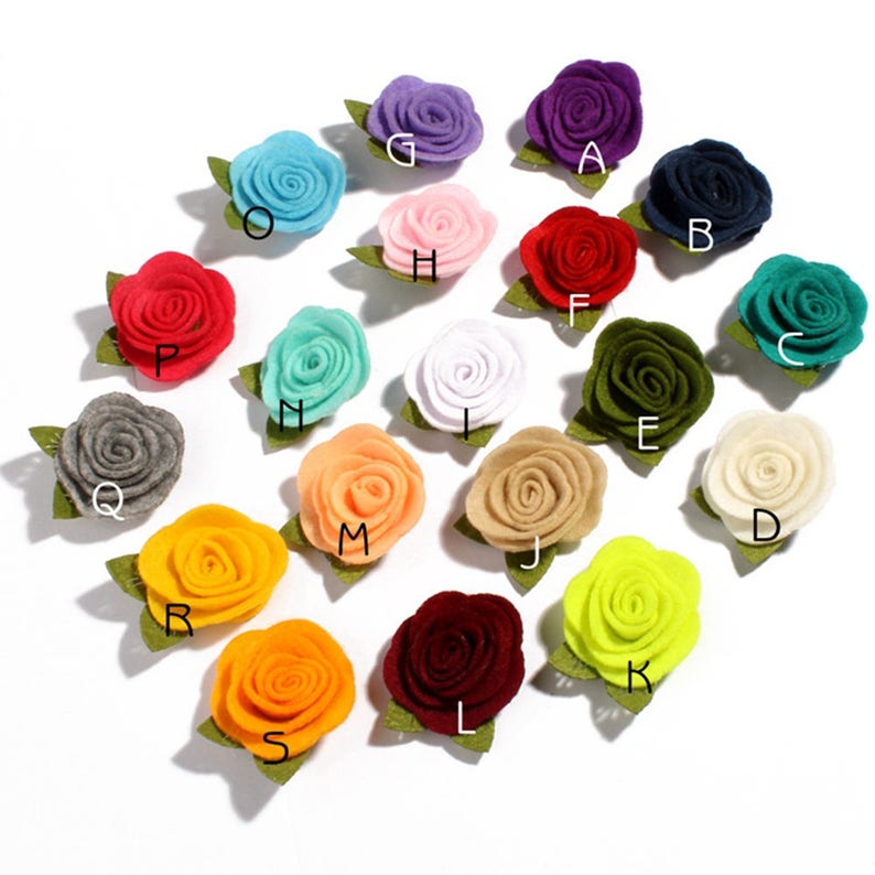 K&ouml;nnte beinhalten: Eine Sammlung bunter Filzrosenbl&uuml;ten mit gr&uuml;nen Bl&auml;ttern. Die Rosen sind in verschiedenen Farbt&ouml;nen gehalten, darunter Rot, Blau, Lila und Gelb. Jede Blume hat eine Buchstabenbezeichnung.