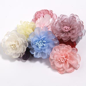 May include: A collection of fabric flowers in various colors, including white, yellow, pink, blue, and mauve. Each flower has multiple layers of delicate petals and a central cluster of small beads. The flowers are arranged together, creating a colorful display.