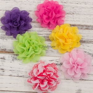 May include: Six fabric flowers in various colors, including purple, green, yellow, pink, and red. The flowers are made of a soft, layered fabric with a lace trim.