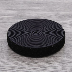 Puede incluir: Un rollo de el&aacute;stico negro con una textura aterciopelada. El el&aacute;stico est&aacute; enrollado apretado y tiene aproximadamente 2,5 cm de ancho.