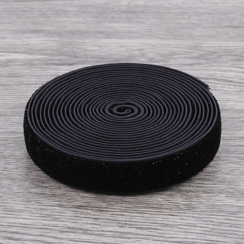 Puede incluir: Un rollo de el&aacute;stico negro con una textura aterciopelada. El el&aacute;stico est&aacute; enrollado apretado y tiene aproximadamente 2,5 cm de ancho.